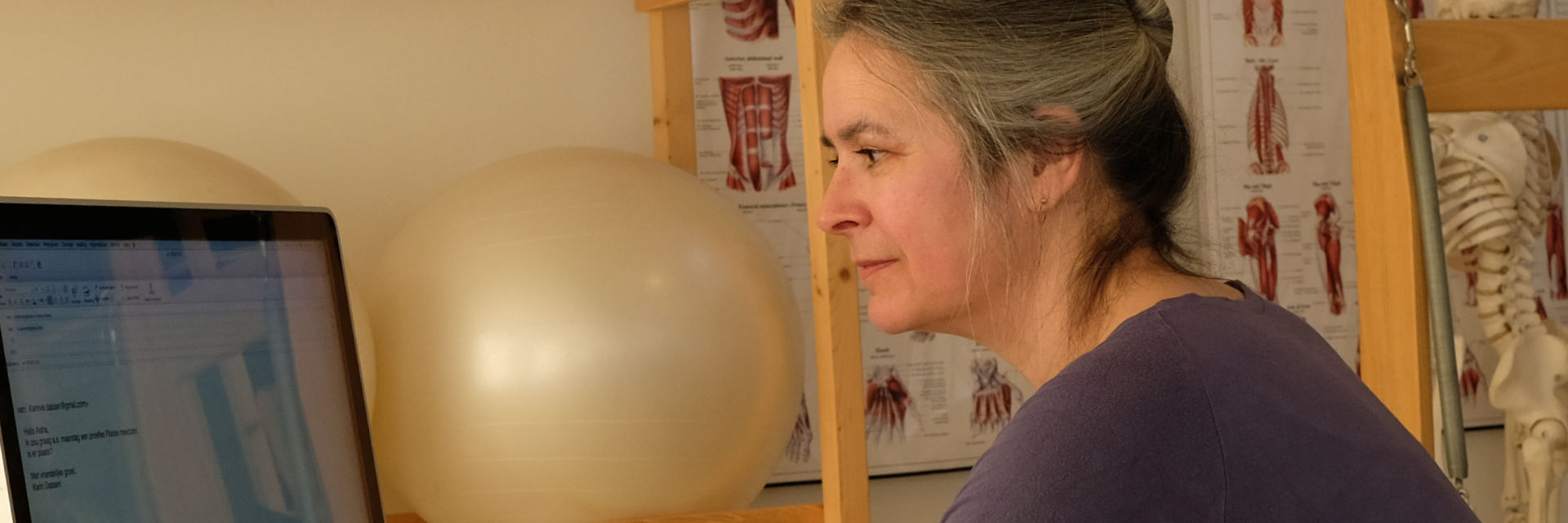 Aisha at the laptop in the studio, with anatomical charts on the wall