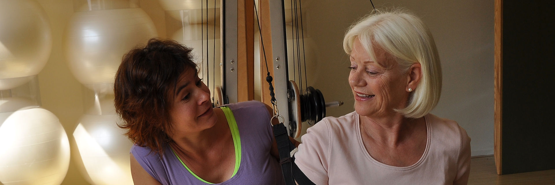 A participant and the trainer smile at each other during an exercise on the pulley tower